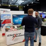 Beratung am Messestand mit laufender Videopräsentation im Hintergrund