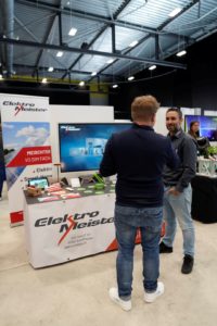Beratung am Messestand mit laufender Videopräsentation im Hintergrund