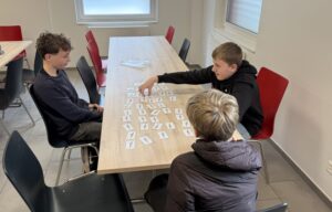 Drei Jugendliche sitzen an einem Tisch und beschäftigen sich mit Karten für eine Berufsorientierungsübung.
