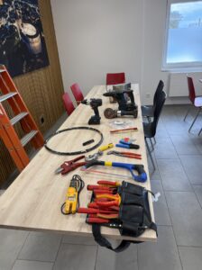 Auf einem Tisch liegen verschiedene Werkzeuge, Messgeräte und Materialien aus dem Bereich Elektroinstallation.
